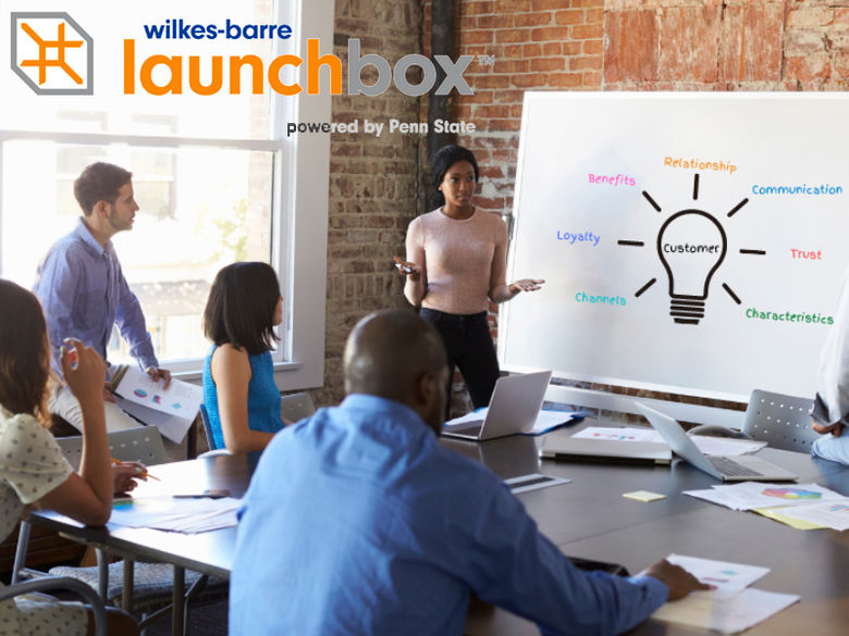 A group of people gathered around a whiteboard with the LaunchBox logo floating in the upper left